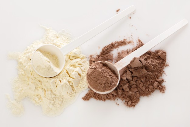 Breastfeeding protein powders on a counter with white plastic spoons on top of the powders.