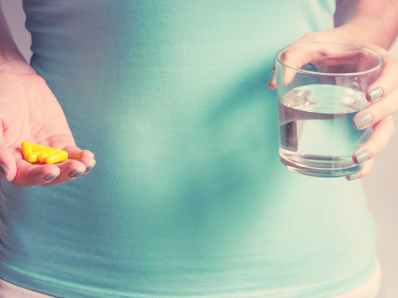 Person holding vitamins and a glass of water. This article discusses the best postnatal vitamins.