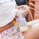Woman pumping breast milk underneath white shirt. This article asks, how many calories does pumping burn?