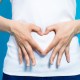 Woman in white shirt making a heart on her gut with her hands. This articles discusses the best probiotics for nursing moms.